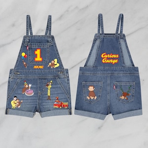 May include: Denim overalls with Curious George graphics. The front features a large yellow number 1, Curious George illustrations, and the word "NAME". The back has "Curious George" text and Curious George graphics.