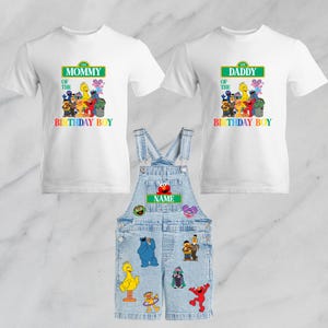 May include: A set of Sesame Street-themed birthday outfits. Includes two white t-shirts, one with "Mommy of the Birthday Boy" and the other with "Daddy of the Birthday Boy". Also, a denim overall with Sesame Street character patches.