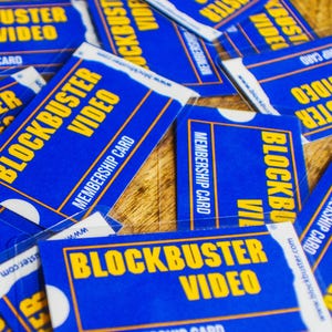 May include: A pile of blue and yellow Blockbuster Video membership cards. Each card displays the Blockbuster logo and the words "Membership Card." The image also includes the text "THE MEMBERSHIP THAT DEFINED A GENERATION - NOW YOURS AGAIN!!"