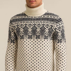 May include: Cream-coloured turtleneck jumper featuring a navy blue geometric pattern across the chest and sleeves. The pattern includes diamond and snowflake-like shapes. Ribbed cuffs and hem complete the design. A classic winter knit.