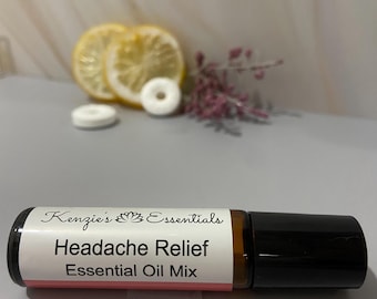 May include: A Headache Relief Essential Oil Mix roll-on bottle with a black cap. The label reads "Kenzie's Essentials" and "Headache Relief Essential Oil Mix." Sliced lemons, white mints, and pink flowers are in the background.