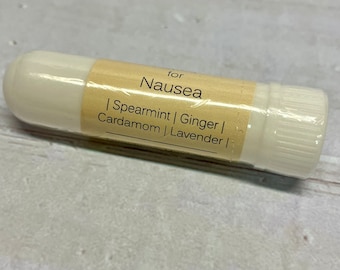 May include: White roll-on essential oil blend for nausea, with the text "for Nausea | Spearmint | Ginger | Cardamom | Lavender |" printed on the label.