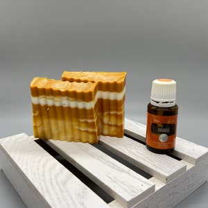 Peut inclure: Deux savons rayés orange et blanc sur une caisse en bois blanche avec une petite bouteille d'huile essentielle d'orange étiquetée "You've Got This" et "Orange".