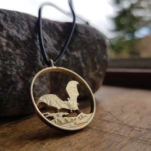 May include: A gold-toned necklace with a round pendant featuring a detailed silhouette of a bat flying over a forest scene.