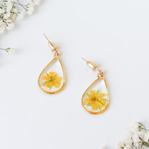 May include: A pair of gold teardrop earrings with a pressed yellow flower inside each earring.