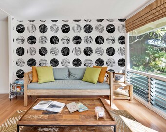 Op de afbeelding: Een woonkamer met een lichtgrijze bank met twee kussens, een salontafel met boeken en een kaars, en een muur met een zwart-wit marmerpatroon behang.