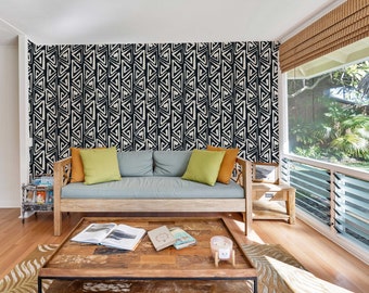 Op de afbeelding: Een woonkamer met een bank en een salontafel. De bank is lichtblauw en de muur erachter is versierd met een zwart-wit geometrisch patroon. De salontafel is van hout en heeft een paar boeken erop.