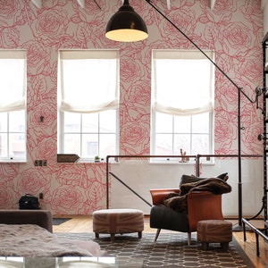 May include: A living room interior with a pink and white floral wallpaper featuring a repeating rose pattern. The room has a large couch, two armchairs, a coffee table, and a bookshelf.