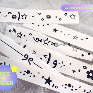 May include: White sticker strips with black graphic designs, including stars, swirls, and emoticons. The text "2 PCS PER ORDER" is visible, along with "20+ colors available". These stickers are ideal for crafting and decorating.