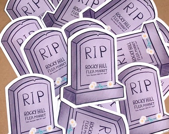 May include: A pile of purple and white tombstone-shaped stickers with the text "RIP" and "Rocky Hill Flea Market" on them. The stickers are designed to look like gravestones with flowers.
