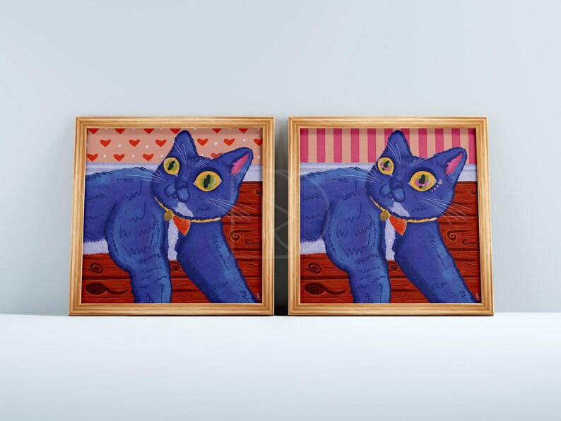 Puede incluir: Dos pinturas enmarcadas de un gato azul con ojos amarillos y un collar rojo. El gato est&aacute; acostado sobre una superficie con estampado rojo y blanco. Los marcos son de madera y tienen un acabado marr&oacute;n claro.
