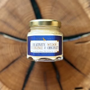May include: A small glass jar candle with a gold lid. The label is blue with gold lettering that reads "CREATIVITY, WISDOM INTELLIGENCE & ORIGINALITY". The label also includes the text "Magical Numbers: 713, 9 3/4, 12, 11, 47 Soy Candle Hand Poured In Texas".