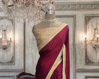 Puede incluir: Un sari de color granate profundo con una tela suave y fluida drapeada sobre un maniquí. La prenda incluye un corpiño dorado ricamente adornado con bordados intrincados y un borde dorado a juego a lo largo de los bordes del drapeado.