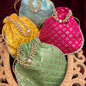 Puede incluir: Cuatro pequeñas bolsas de cordón con ribete de perlas. Las bolsas están hechas de una tela con un patrón floral y son de color azul, amarillo, rosa y verde.