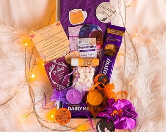 May include: A purple and white gift box filled with Halloween themed items, including a Cadbury chocolate bar, a face mask, a lip balm, and a small bag of marshmallows. The box is decorated with a witching hour sign and a spooky Halloween checklist.