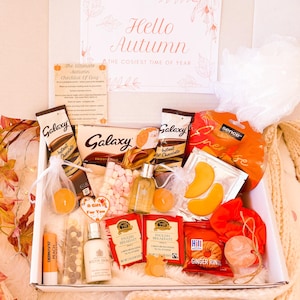 May include: A gift box with autumn-themed items, including Galaxy chocolate, instant hot chocolate sachets, English Breakfast tea bags, and ginger rings. The box is decorated with a card that reads "Hello Autumn, The Cosiest Time of Year".