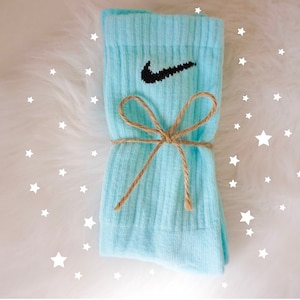 May include: A pair of light blue socks with the Nike swoosh logo in black. The socks are tied with a brown twine bow. The background is white with white star shapes.