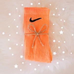 May include: A pair of orange socks with the Nike swoosh logo in black. The socks are tied with twine in a bow. The background is white with white star shapes.