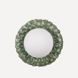 Pode incluir: Uma arandela de parede de cerâmica verde e marrom com um globo de vidro branco fosco no centro. A arandela tem um design floral texturizado.