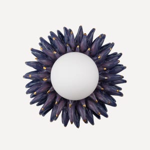 Pode incluir: Uma arandela de parede de cerâmica com um globo branco no centro. A arandela tem a forma de uma flor com pétalas roxas e detalhes dourados.