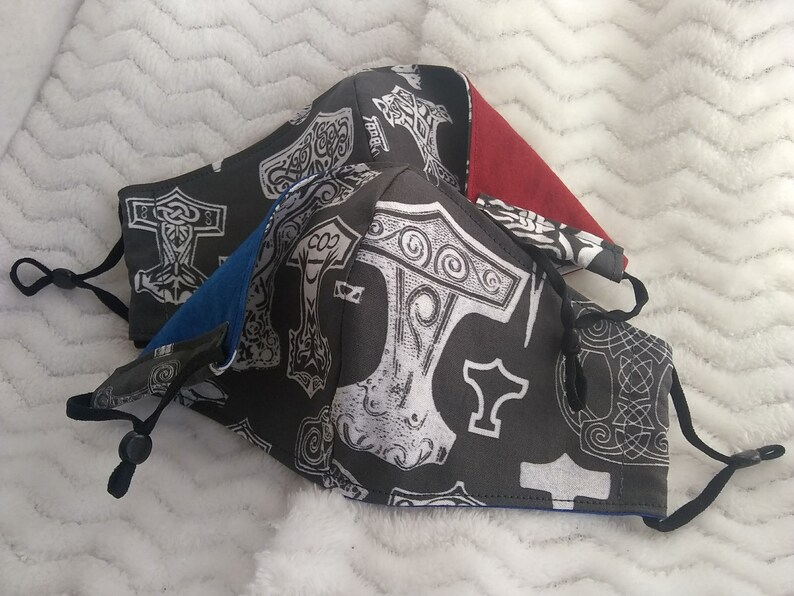 May include: Three face masks with black fabric and white Mjolnir hammer designs. The masks have black elastic straps. One mask has a red fabric lining, one has a blue fabric lining, and one has a gray fabric lining.