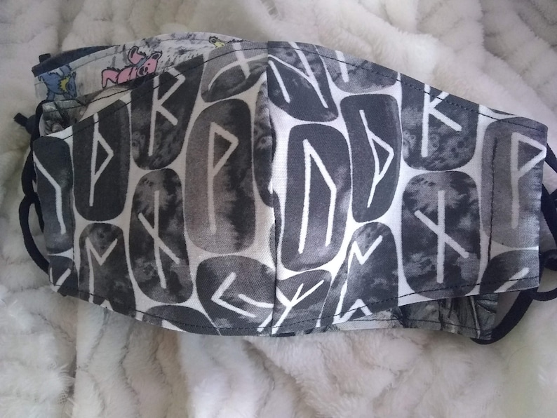 May include: A black and white face mask with a pattern of runes. The runes are in a stylized font and are arranged in a repeating pattern.