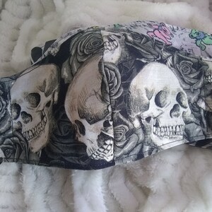 May include: Black face mask with a skull and rose design. The mask features three white skulls with black eyes and a black background with white roses.