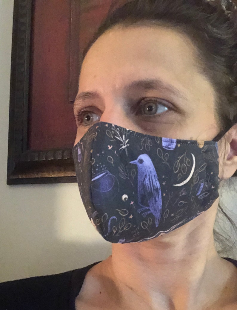 May include: A person wearing a black face mask with a purple bird, stars, and other whimsical designs.
