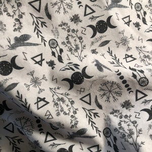 May include: A white fabric with a black and white repeating pattern of various symbols, including moons, triangles, and a compass rose. The fabric has a subtle texture.