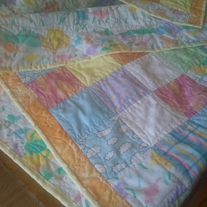 May include: A patchwork quilt with a variety of pastel colors and patterns, including floral, geometric, and cloud designs. The quilt is edged with a yellow border.