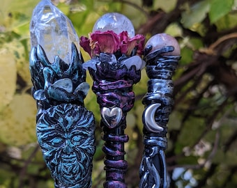 May include: Three decorative wands with different crystal tops. The first wand has a clear crystal top with a green and black design. The second wand has a clear crystal top with a pink flower and a purple and black design. The third wand has a pink crystal top with a black and silver design.
