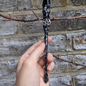 May include: Black and silver wand with a pentagram charm. The wand is made of resin and has a textured surface.