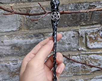 May include: Black and silver wand with a pentagram charm. The wand is made of resin and has a textured surface.