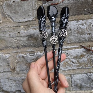 May include: Three black wands with silver pentagram charms and black gemstone tips. The wands are made of a black and silver material that resembles tree bark.