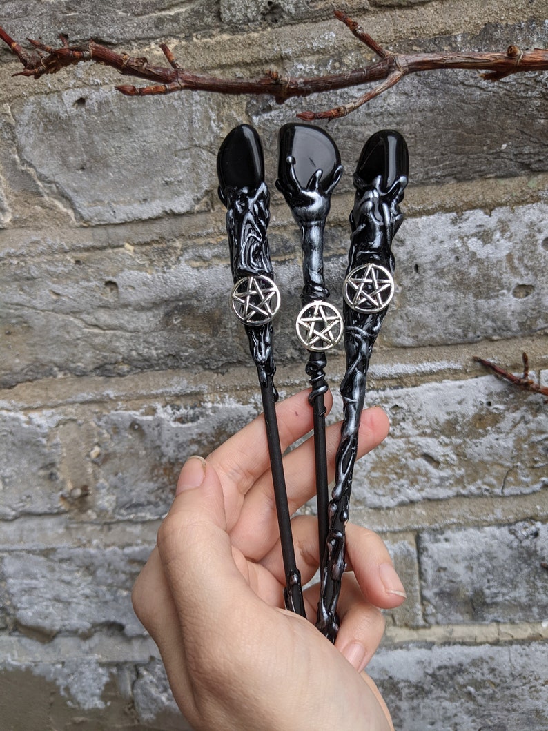 May include: Three black wands with silver pentagram charms and black gemstone tips. The wands are made of a black and silver material that resembles tree bark.