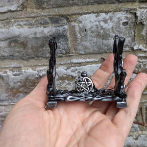 May include: Black metal crystal stand with a pentagram design. The stand has a base and two vertical supports.