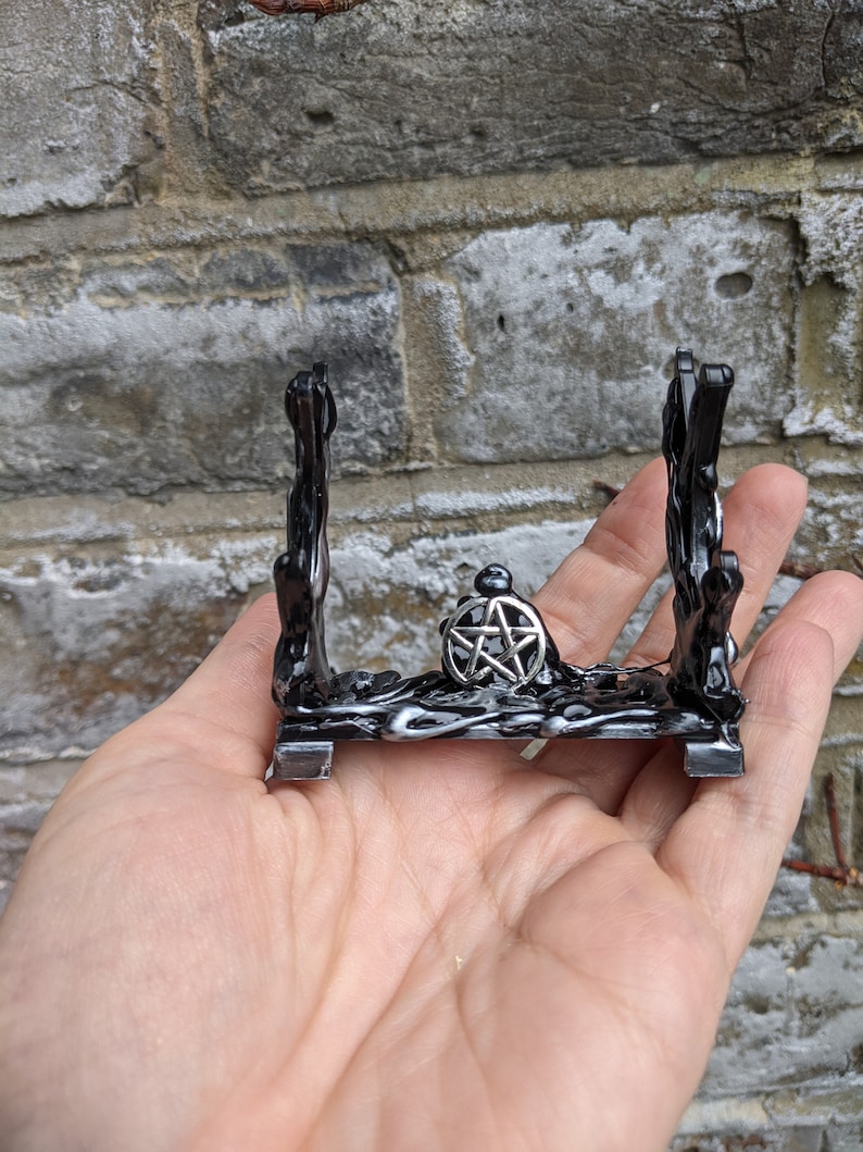 May include: Black metal crystal stand with a pentagram design. The stand has a base and two vertical supports.