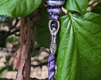 May include: A purple heart-shaped amethyst crystal is attached to a black and purple wand with silver accents. The wand has a silver charm of a woman with a spiral design.