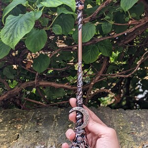 May include: A copper-toned wand with a clear quartz crystal at the top and a crescent moon charm. The wand is decorated with intricate details and has a clear quartz crystal at the base.