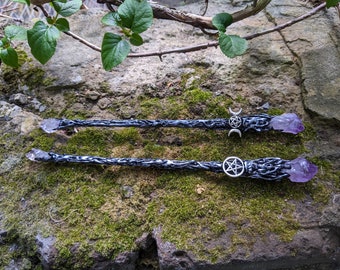 May include: Two black wands with amethyst crystal tips and silver pentagram and crescent moon charms. The wands are lying on a bed of moss.