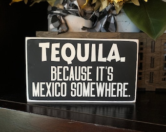 May include: Black wooden sign with white text that reads "Tequila. Because it's Mexico somewhere."