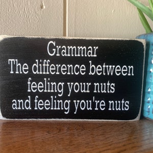 May include: Black wooden sign with white text that reads "Grammar: The difference between feeling your nuts and feeling you're nuts."