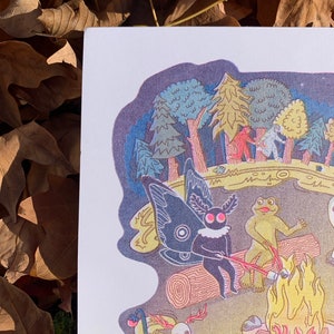 May include: A whimsical illustration of a campfire scene with a skeleton, a frog, and a moth with large, black wings. The scene is set in a forest at night with a starry sky. The characters are gathered around a campfire, roasting marshmallows.