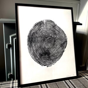 May include: Black and white print of a tree trunk cross-section, showing the rings. The print is framed in a black frame and is hanging on a wall.