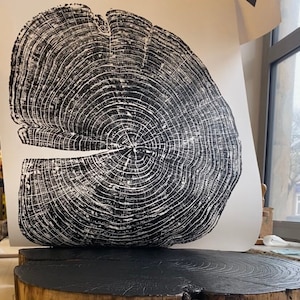 May include: A black and white print of a tree trunk cross section with visible growth rings. The print is displayed on a dark wood slice.