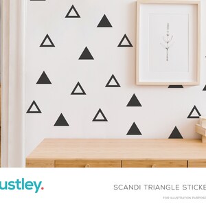 Puede incluir: Pared blanca decorada con pegatinas de triángulos negros. Una impresión botánica enmarcada cuelga sobre un escritorio de madera. El texto "SCANDI TRIANGLE STICKERS" y la marca "austley" son visibles en la parte inferior.