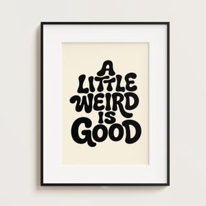 May include: Black framed art print with the phrase "A Little Weird Is Good" in a bold, retro font. The text is in black against a cream-colored background. The artwork is a framed wall decor piece.