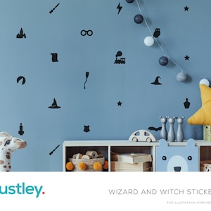 Könnte beinhalten: Eine blaue Wand, verziert mit schwarzen Aufklebern zum Thema Zauberer und Hexen, darunter ein Zauberstab, ein Hut und Sterne. Ein Giraffenspielzeug und Holzspielzeug befinden sich auf einem weißen Regal. Der Text "WIZARD AND WITCH STICKERS" steht unten.