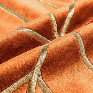 K&ouml;nnte beinhalten: Nahaufnahme eines rostfarbenen Stoffes mit goldener Stickerei. Der Stoff hat eine weiche, samtige Textur und ein geometrisches Muster.