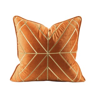 K&ouml;nnte beinhalten: Ein orangefarbenes Samtkissen mit einem geometrischen Muster aus goldenen Stickereien.